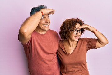 Poster - Beautiful middle age couple together wearing casual clothes very happy and smiling looking far away with hand over head. searching concept.