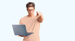 © Krakenimages.com - Young handsome man wearing glasses holding laptop pointing with finger to the camera and to you, confident gesture looking serious