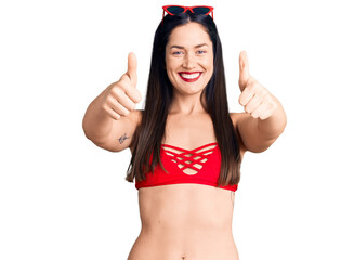 Poster - Young beautiful caucasian woman wearing bikini approving doing positive gesture with hand, thumbs up smiling and happy for success. winner gesture.