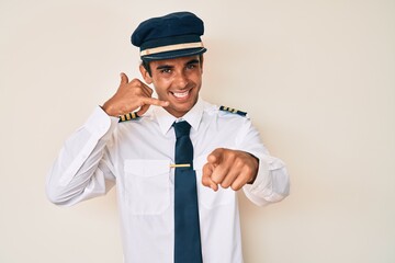 Sticker - Young hispanic man wearing airplane pilot uniform smiling doing talking on the telephone gesture and pointing to you. call me.