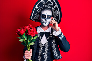 Sticker - Young man wearing mexican day of the dead costume holding roses serious face thinking about question with hand on chin, thoughtful about confusing idea