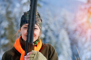 Wall Mural - A young beautiful hunter woman on hunt in forest with rifle on the shoulder. Winter season. Copy space for text