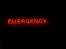 A Signboard Showing Red Letters "EMERGENCY" And A Dark Background.