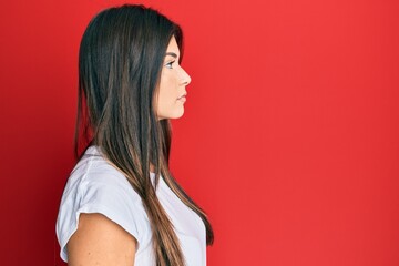 Poster - Young brunette woman wearing casual white tshirt over red background looking to side, relax profile pose with natural face with confident smile.