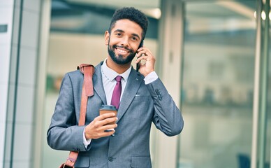 Poster - Young african american businessman talking on the smartphone and drinking take away coffee at the city.