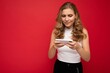 © Ivan Traimak - Photo of concentrated beautiful young blonde woman wearing white t-shirt isolated on red background using smartphone and playing phone games looking at gadjet screen