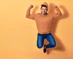 Young handsome latin man wearing casual clothes smiling happy. Jumping with smile on face over isolated yellow background