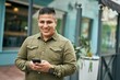 Young latin man smiling happy using smartphone at the city.