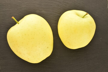 Two ripe yellow apples, close-up, on a slate board.