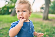 Sad Little Boy Putting Fingers On Mouth Touching Gums Because Toothache At The Park On A Sunny Day. Beautiful Blonde Hair Male Toddler In Pain For New Baby Teeth Outdoors