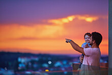 Happy Father And Baby Watching The City On Sunset At The Rooftop Balcony With Glass Balustrade