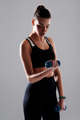 Athletic woman wearing sports wear doing physical exercise using dumbbell, isolated background. Sport and healthcare concept