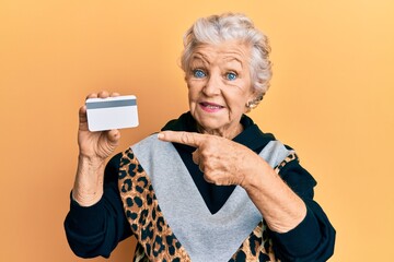 senior grey-haired woman holding credit card smiling happy pointing with hand and finger
