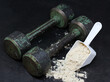 Dry protein in a spoon and old iron dumbbells.