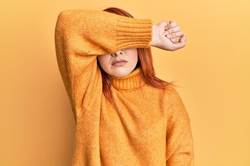 Wall Mural - Beautiful redhead woman wearing casual winter sweater over yellow background covering eyes with arm, looking serious and sad. sightless, hiding and rejection concept