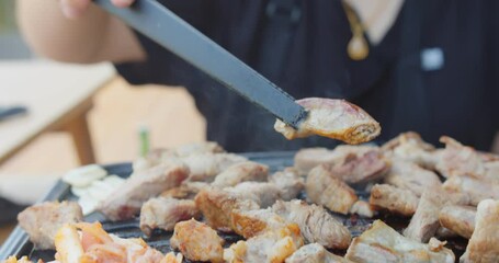 Wall Mural - Person roasting grilling holding juicy yummy meat steak with tongs on gas stove plate , Korean style food