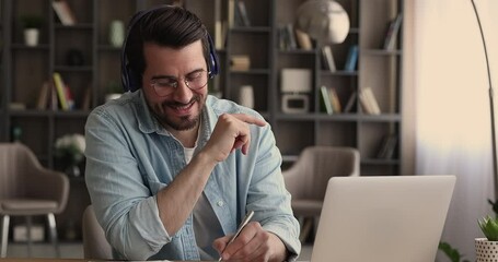 Wall Mural - Man wearing headphones making notes, e learns with on-line tutor by video call. Businessman take part in webinar business virtual meeting work on project with colleagues use laptop and video call app