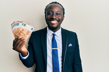 Poster - Handsome young black man wearing business suit holding 50 euros banknotes looking positive and happy standing and smiling with a confident smile showing teeth