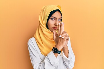 Sticker - Young brunette arab woman wearing traditional islamic hijab scarf holding symbolic gun with hand gesture, playing killing shooting weapons, angry face