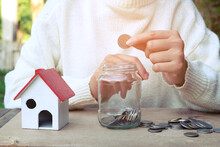 Midsection Of Woman Putting Coin In Jar Model House On Table