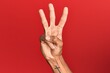 © Krakenimages.com - Hand of hispanic man over red isolated background counting number 3 showing three fingers