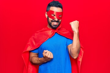 Poster - Young hispanic man wearing super hero costume celebrating surprised and amazed for success with arms raised and eyes closed