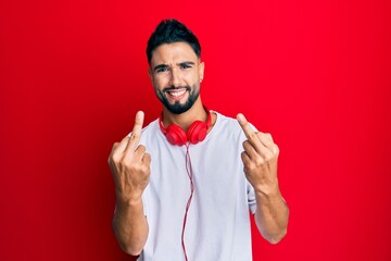 Poster - Young man with beard listening to music using headphones showing middle finger doing fuck you bad expression, provocation and rude attitude. screaming excited