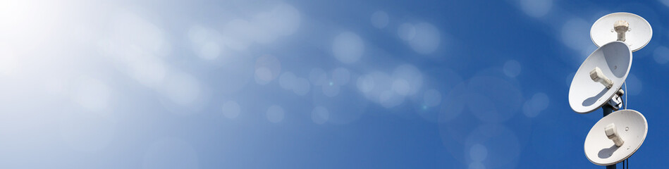 Several telecommunications antennas of a cellular network and wireless internet against a blue sky. Receiving and digitizing multiple pieces of information at once. Panoramic frame. Blue background.