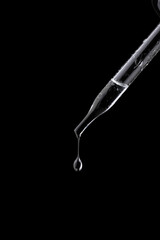 Glass pipette with drop on black background