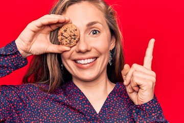 Canvas Print - Young beautiful blonde woman holding chocolate chips cookie smiling happy pointing with hand and finger to the side