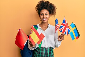 Beautiful african american woman with afro hair exchange student holding countries flags smiling with a happy and cool smile on face. showing teeth.