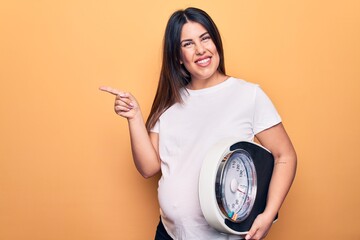 Sticker - Young beautiful brunette pregnant woman holding controlling weight using weighting machine smiling happy pointing with hand and finger to the side