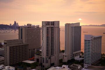 Wall Mural - Pattaya city at chon buri in thailand on sunset or morning sunrise and warm sun light on orange sea water with boat and tower building or hotel by real estate business for holiday travel on golden sky