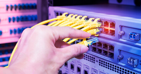 Wall Mural - hand holding network cable on the switch hub in server room background