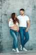 © Aliaksandr Marko - A pregnant girl and her husband are standing against the wall. Beautiful belly of a young attractive pregnant girl. Family, marriage, childbirth concept.