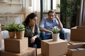 Fototapete - Unhappy young Caucasian man and woman sit on couch argue quarrel on moving day to new home. Distressed upset millennial couple renters have family misunderstanding relocating unpacking.