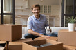 Portrait of smiling millennial man wrap cardboard packages using adhesive scotch, feel excited relocating to new house. Happy young Caucasian male renter pack boxes with belonging with tape dispenser.