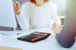© Iryna - Accountant checking financial statement or counting by calculator income for tax form, hands close-up. Business woman sitting and working with colleague at the desk in office. Audit concept
