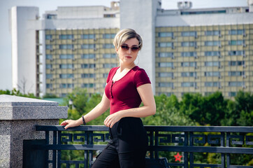 Wall Mural - A girl with glasses stands next to a metal fence against the background of buildings