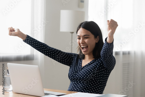 Overjoyed millennial vietnamese korean woman raising arms in air, celebrating getting email with unexpected good news, online lottery win notification, dream job offer or last banking payment notice.