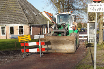 Wheel bulldozer with bucket at street in the Dutch village of Bergen during construction of the road. Traffic signs with: Doorgaand verkeer afgesloten (Closed through traffic) and Uitgezonderd (except