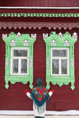 Wall Mural - Russian woman in traditional national Pavlovo Posad scarf, shawl. Folk style in architectural fashion, architecture. Vintage wooden rural house, ornamental windows in Nerekhta, Ivanovo region, Russia