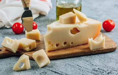 Piece of cow's milk Maasdam cheese on wooden cutting board over concrete bsckground.