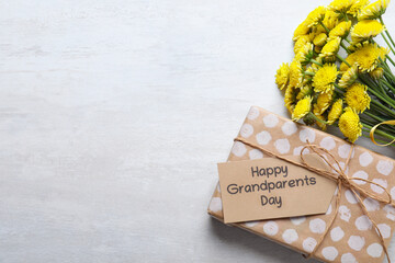 Canvas Print - Beautiful yellow flowers, gift box and tag with phrase Happy Grandparents Day on light background, flat lay. Space for text