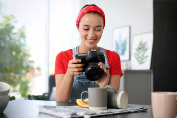 Poster - Young photographer taking picture of cups at table indoors, focus on camera