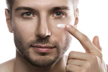 Men's beauty. Young man is applying moisturizing and anti aging cream on his face