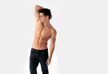 Sexy young man with nacked torso in black jeans, posing in studio with his hand raised, isolated on a white background.