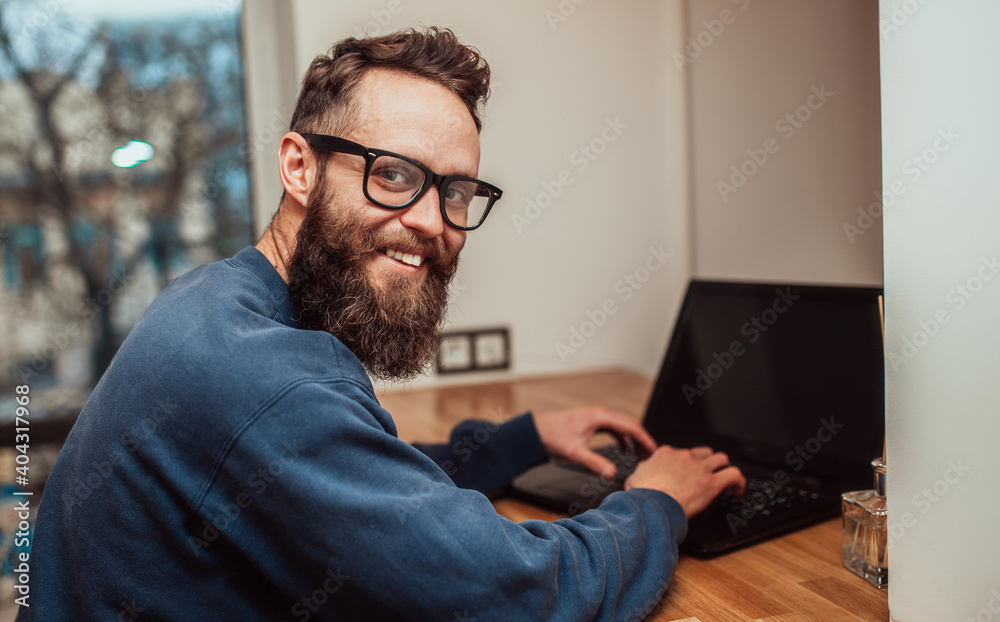 A young modern man works at a laptop from home using high-speed wi-fi ...