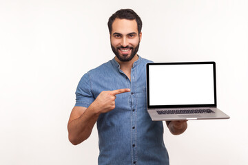 Wall Mural - Cheerful positive man pointing finger showing empty display of laptop, blogger presenting freespace, advertising area. Indoor studio shot isolated on white background