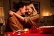 © insta_photos - Happy smiling affectionate young couple in love hugging laughing, drinking wine, talking, celebrating Valentines day dining together, having romantic dinner date in candle light sitting at home table.